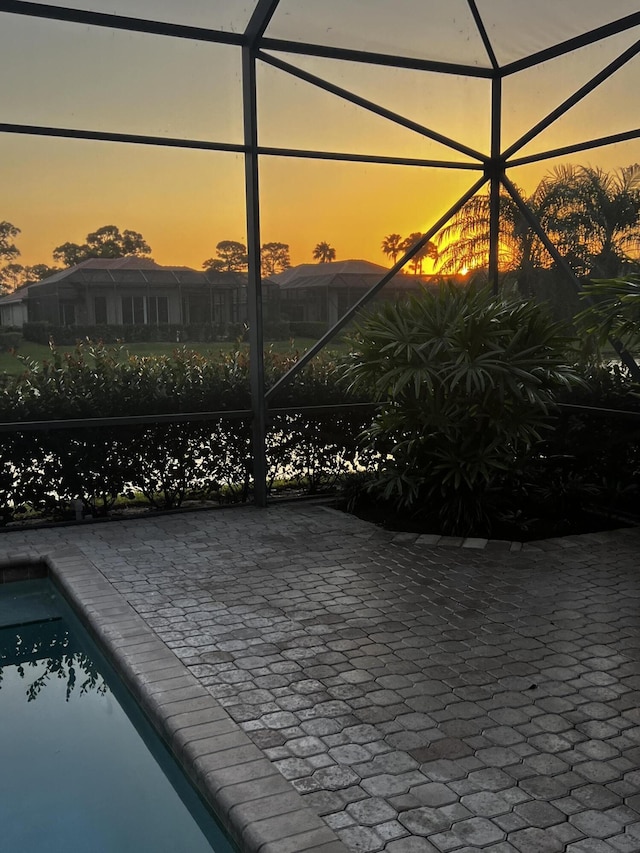 pool at dusk featuring a patio area, glass enclosure, and an outdoor pool