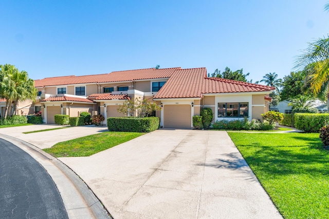 mediterranean / spanish home featuring an attached garage, a tiled roof, concrete driveway, stucco siding, and a front lawn