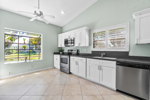 kitchen with dark countertops, vaulted ceiling, stainless steel appliances, a sink, and light tile patterned flooring