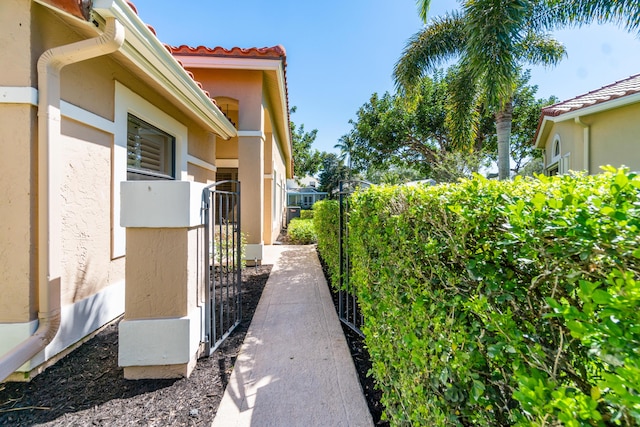 view of side of property with fence, a tile roof, a gate, and stucco siding