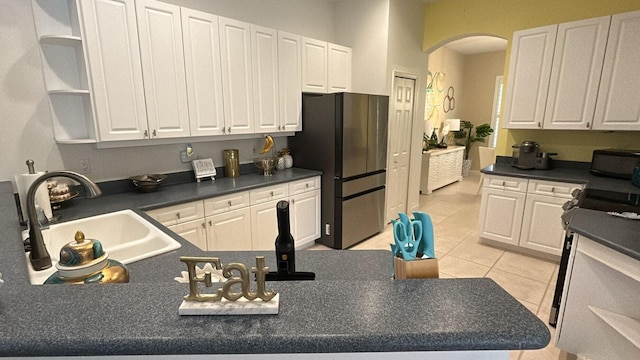 kitchen featuring open shelves, light tile patterned floors, freestanding refrigerator, white cabinets, and a sink