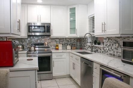 kitchen featuring stainless steel appliances, white cabinets, a sink, and light tile patterned floors