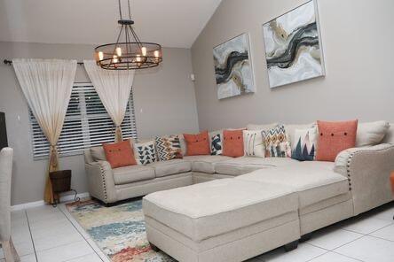 living area featuring light tile patterned floors, vaulted ceiling, baseboards, and an inviting chandelier