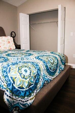 bedroom with baseboards, vaulted ceiling, a closet, and wood finished floors