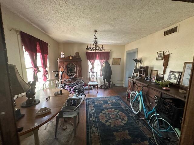 dining room with visible vents, a textured ceiling, an inviting chandelier, and wood finished floors