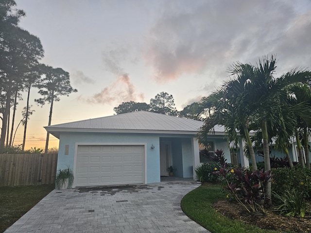 ranch-style home featuring decorative driveway, stucco siding, fence, metal roof, and a garage