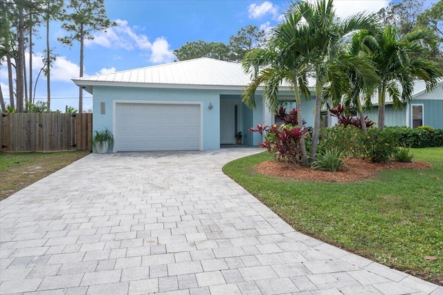 ranch-style home with decorative driveway, stucco siding, an attached garage, metal roof, and fence