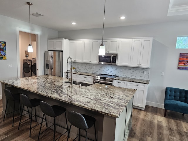 kitchen featuring washing machine and clothes dryer, stainless steel appliances, tasteful backsplash, dark wood-type flooring, and a sink