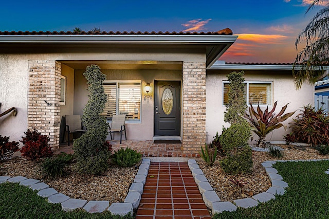 exterior entry at dusk featuring covered porch and stucco siding