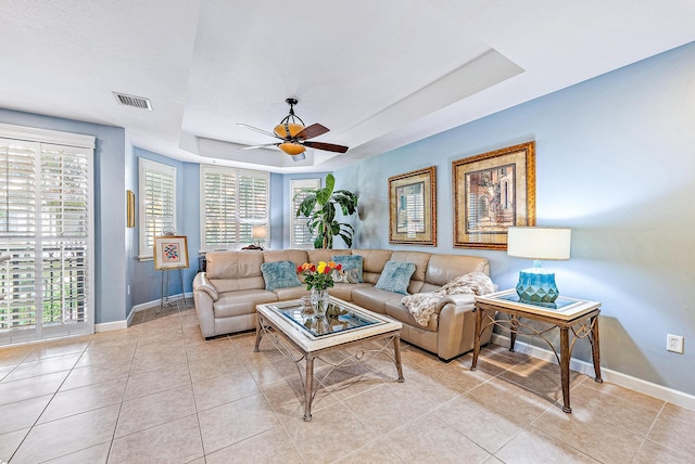 living area featuring light tile patterned floors, a tray ceiling, visible vents, and baseboards