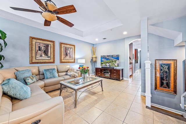 living room featuring light tile patterned floors, arched walkways, a ceiling fan, baseboards, and a raised ceiling