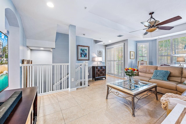 living area with visible vents, baseboards, ceiling fan, a tray ceiling, and light tile patterned flooring