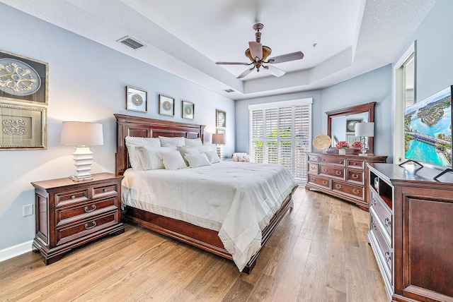 bedroom with light wood finished floors, baseboards, visible vents, a raised ceiling, and a ceiling fan