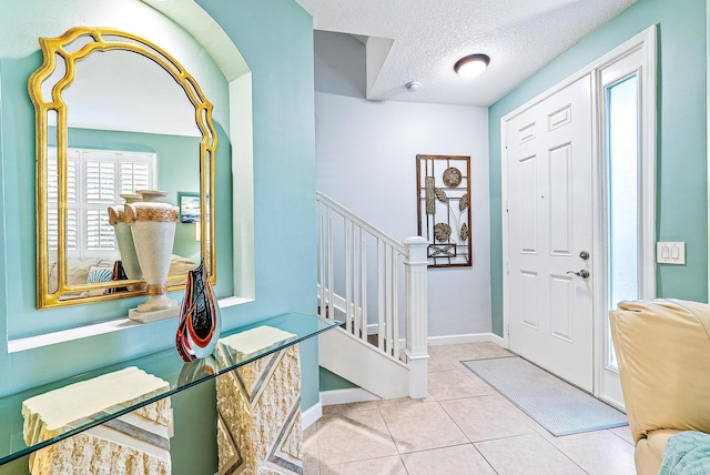 foyer with stairway, baseboards, a textured ceiling, and tile patterned floors