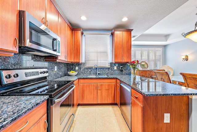 kitchen with stainless steel appliances, light tile patterned flooring, a sink, dark stone counters, and a peninsula