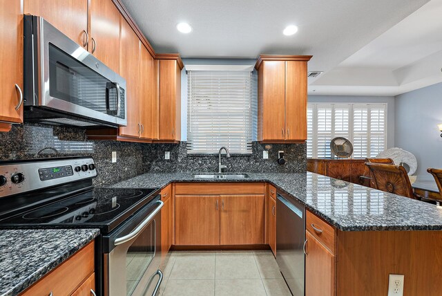 kitchen with decorative backsplash, brown cabinetry, light tile patterned flooring, a textured ceiling, and dark stone countertops