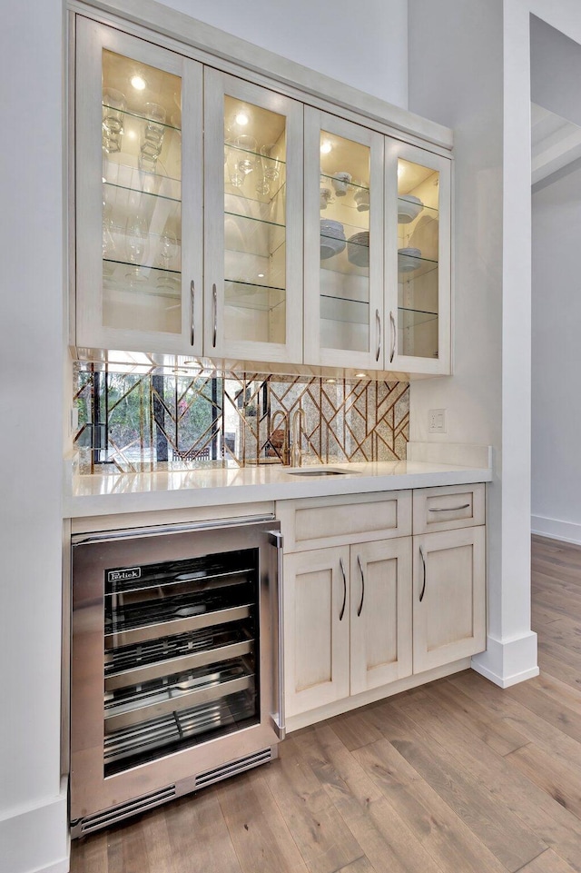 bar featuring beverage cooler, light wood-type flooring, a sink, and baseboards