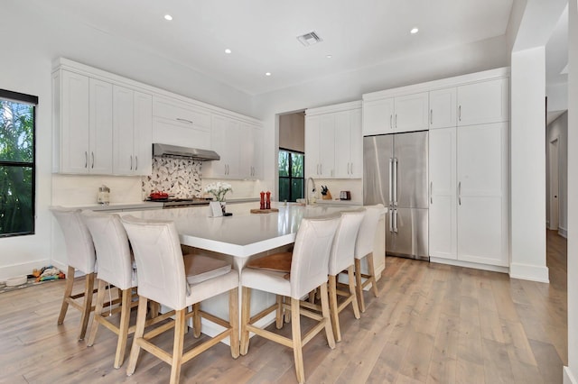 kitchen featuring light wood finished floors, high end refrigerator, visible vents, under cabinet range hood, and backsplash