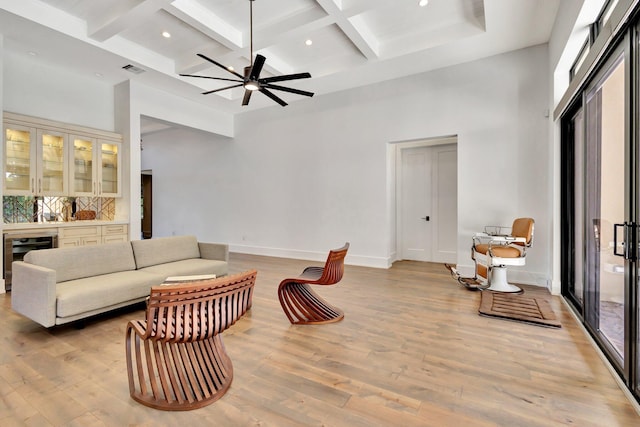 living area with beverage cooler, baseboards, a towering ceiling, light wood-type flooring, and beam ceiling