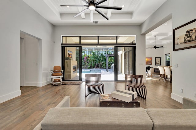 living area with baseboards, visible vents, ceiling fan, wood finished floors, and a high ceiling