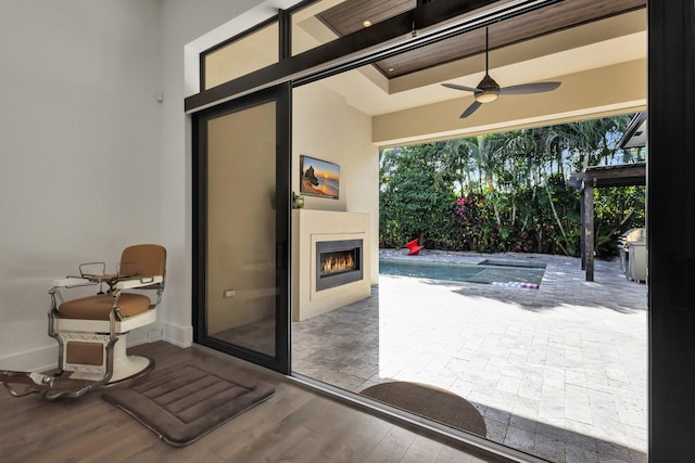 doorway featuring a lit fireplace, ceiling fan, and wood finished floors