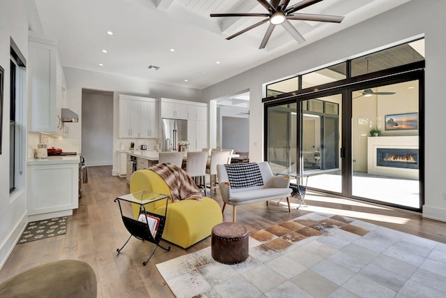 interior space featuring light wood finished floors, recessed lighting, a glass covered fireplace, ceiling fan, and beamed ceiling