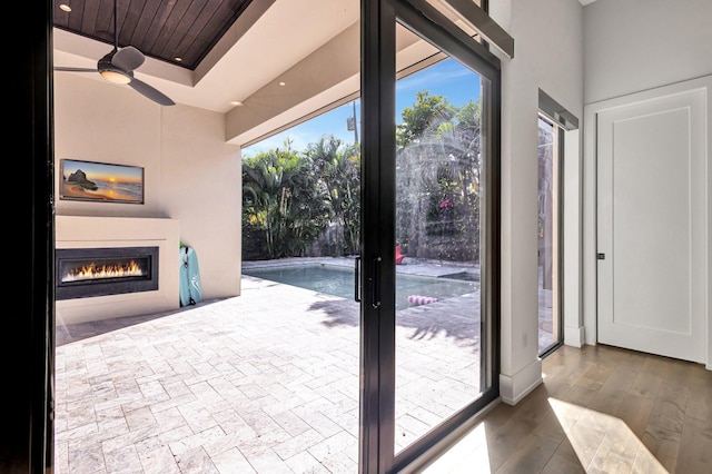 entryway with a wealth of natural light, a glass covered fireplace, ceiling fan, and wood finished floors