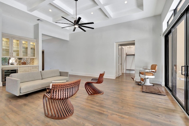 living area with wine cooler, beam ceiling, a high ceiling, and wood finished floors