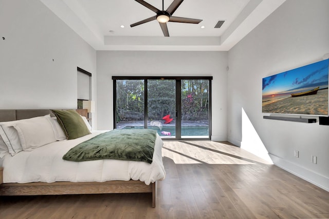 bedroom with access to exterior, a raised ceiling, visible vents, wood finished floors, and baseboards