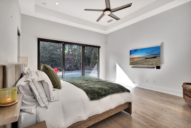 bedroom with a tray ceiling, recessed lighting, baseboards, and wood finished floors