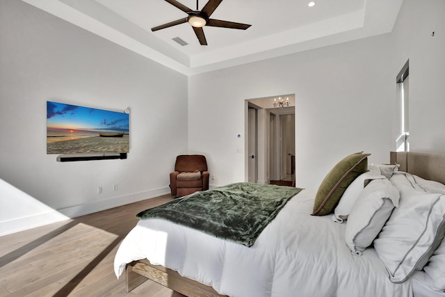 bedroom featuring baseboards, visible vents, a tray ceiling, and wood finished floors