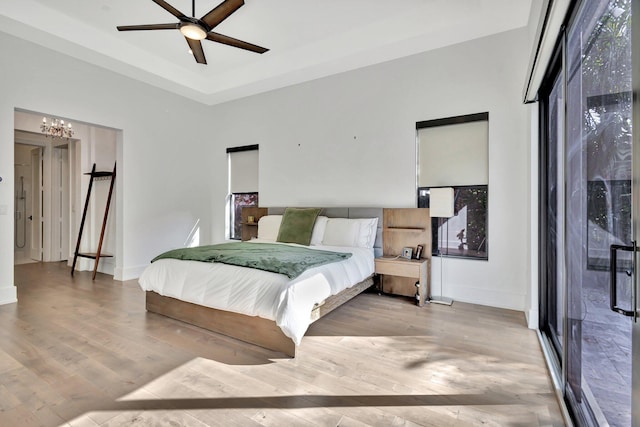 bedroom with baseboards, wood finished floors, access to outside, a tray ceiling, and ceiling fan with notable chandelier