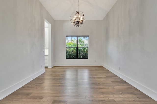 unfurnished room with an inviting chandelier, wood finished floors, and baseboards