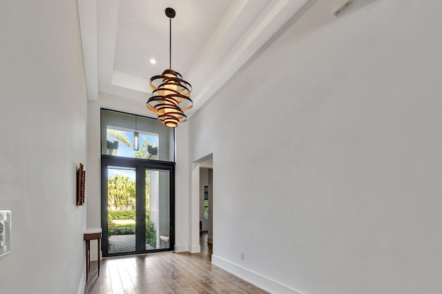 foyer entrance featuring baseboards, a towering ceiling, wood finished floors, a tray ceiling, and a notable chandelier