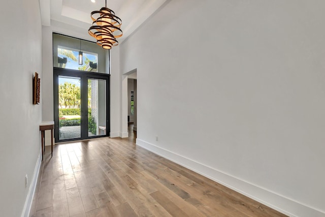 entrance foyer with a chandelier, wood finished floors, a towering ceiling, baseboards, and a tray ceiling