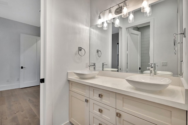 full bathroom featuring double vanity, a sink, baseboards, and wood finished floors