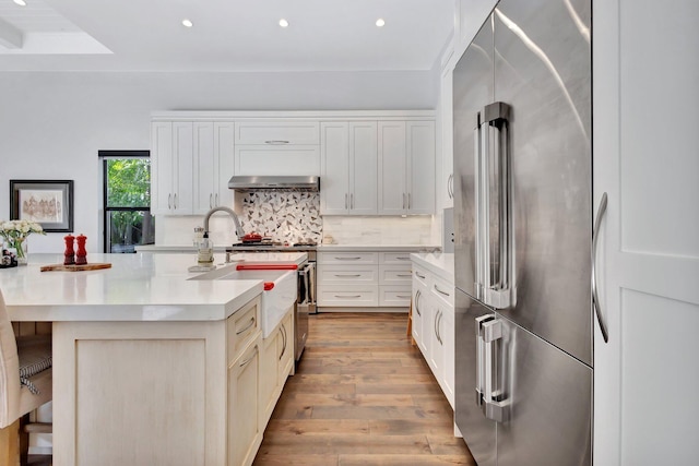 kitchen with extractor fan, light wood-style flooring, high end refrigerator, light countertops, and tasteful backsplash