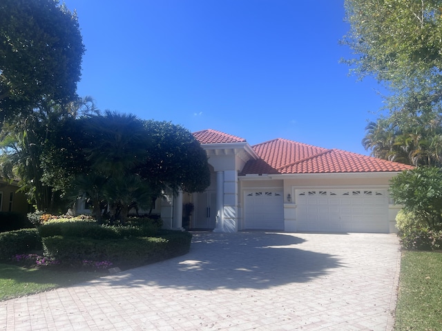 mediterranean / spanish house featuring an attached garage, stucco siding, decorative driveway, and a tiled roof