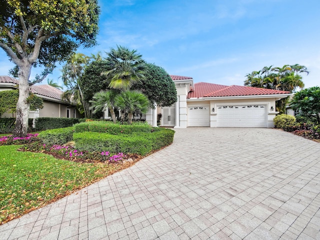 mediterranean / spanish home featuring decorative driveway, a tiled roof, an attached garage, and stucco siding