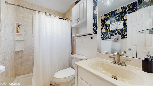 bathroom with toilet, a tile shower, and vanity