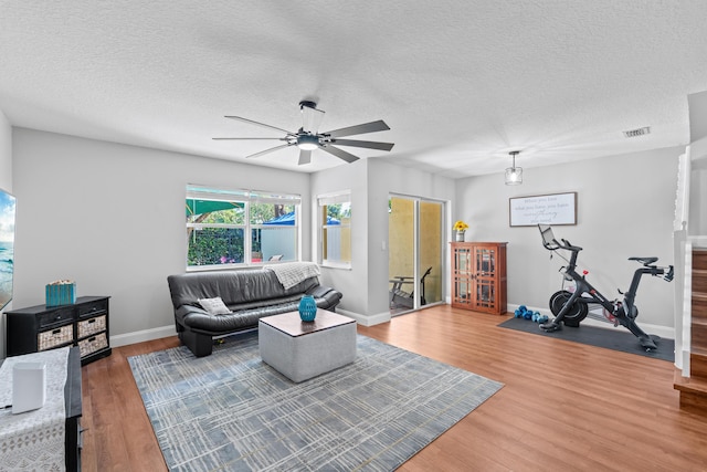 living area with a textured ceiling, wood finished floors, visible vents, and baseboards