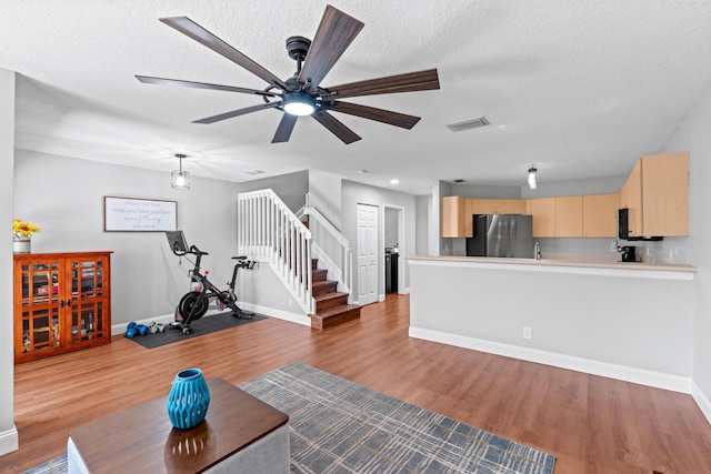 unfurnished living room featuring a textured ceiling, wood finished floors, visible vents, baseboards, and stairway