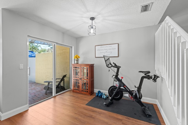 exercise area featuring a textured ceiling, wood finished floors, visible vents, and baseboards