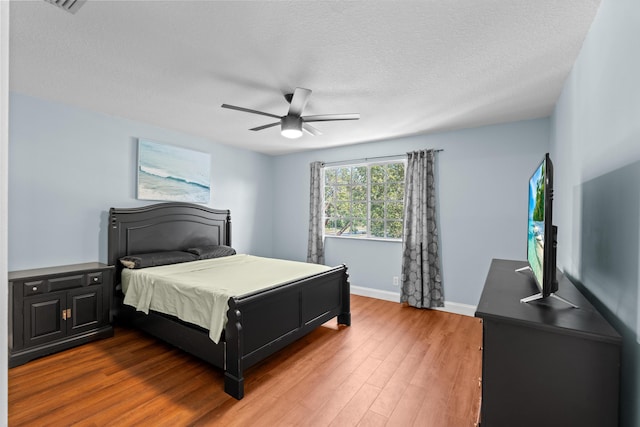 bedroom with a ceiling fan, a textured ceiling, baseboards, and wood finished floors