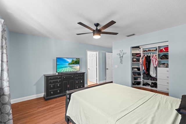 bedroom with ceiling fan, wood finished floors, visible vents, baseboards, and a closet