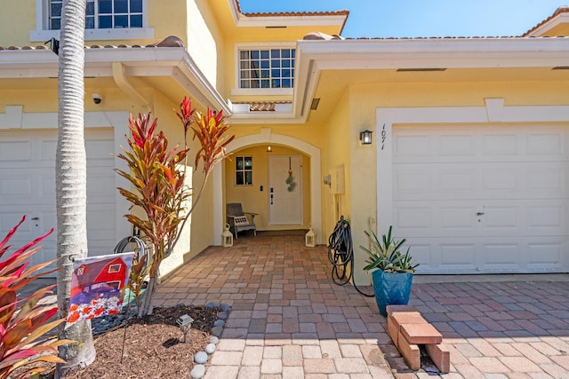 doorway to property with a garage, a tiled roof, and stucco siding