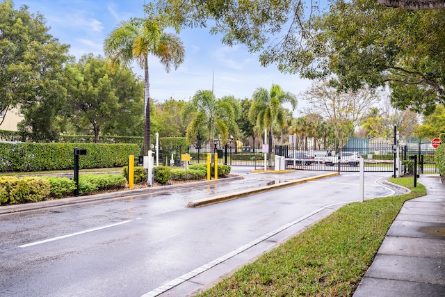 view of road featuring a gated entry, sidewalks, curbs, a gate, and traffic signs