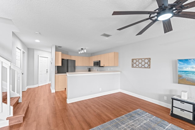 kitchen featuring visible vents, stainless steel microwave, freestanding refrigerator, a peninsula, and light brown cabinetry