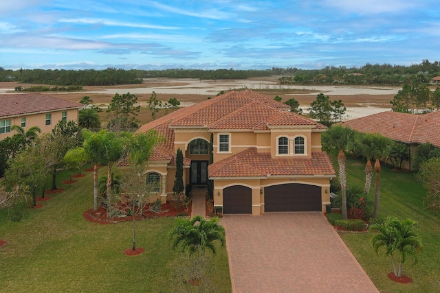 mediterranean / spanish-style house with a garage, a tile roof, decorative driveway, stucco siding, and a front yard