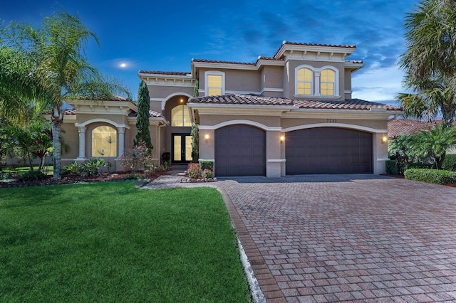 mediterranean / spanish house with a garage, a tiled roof, decorative driveway, stucco siding, and a front lawn